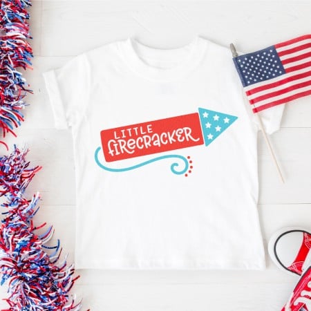 America flag, red tennis shoes, a red, white and blue lei and a white t-shirt with a firecracker image, that says, "Little Firecracker"