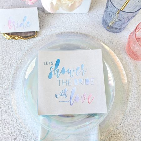 A table setting with a note on the plate that says, "Let's Shower the Bride with Love"