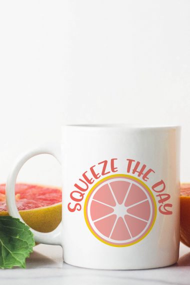 A grapefruit cut in half and a cup of coffee that has an image of a half of a grapefruit and the saying, 'Squeeze the Day"