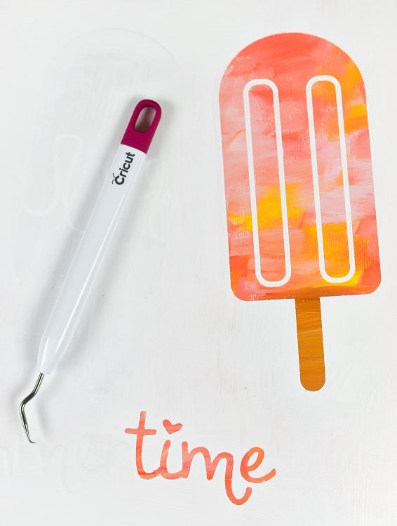 A Crciut weeding tool lying on top of a white canvas with the word 'time' and an image of a popsicle displaying