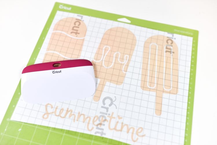 A close up of a Cricut brayer tool laying on top of a Cricut mat that has a cut file of three popsicle images and the word summertime on it