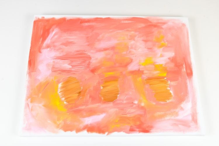 A close up of a white canvas painted with swirls and blended colors of orange, light orange and yellow paint