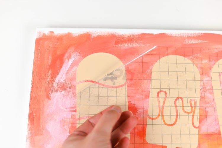 A hand pulling transfer tape off of a painted canvas