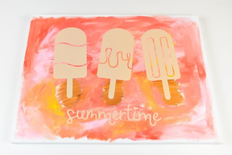A cut file pattern of three popsicles and the word summertime laying over top of a painted canvas