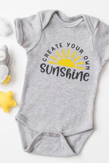 A gray onesie with an image of half of the sun and the saying, "Create Your Own Sunshine"