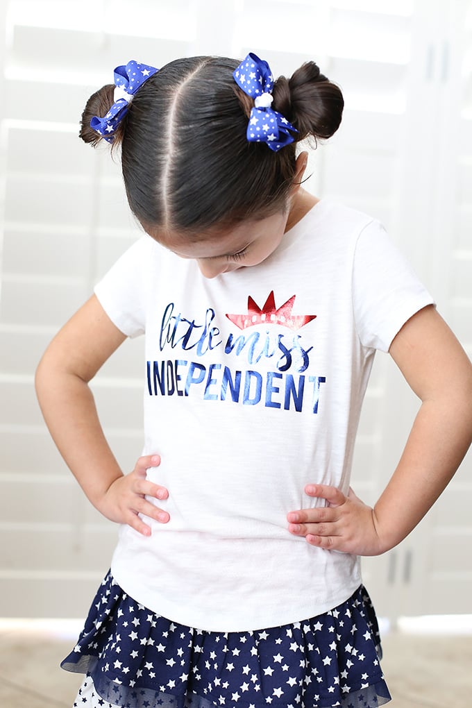 A girl wearing a blue skirt with white stars on it and a white t-shirt that says, "Little Miss Independent"