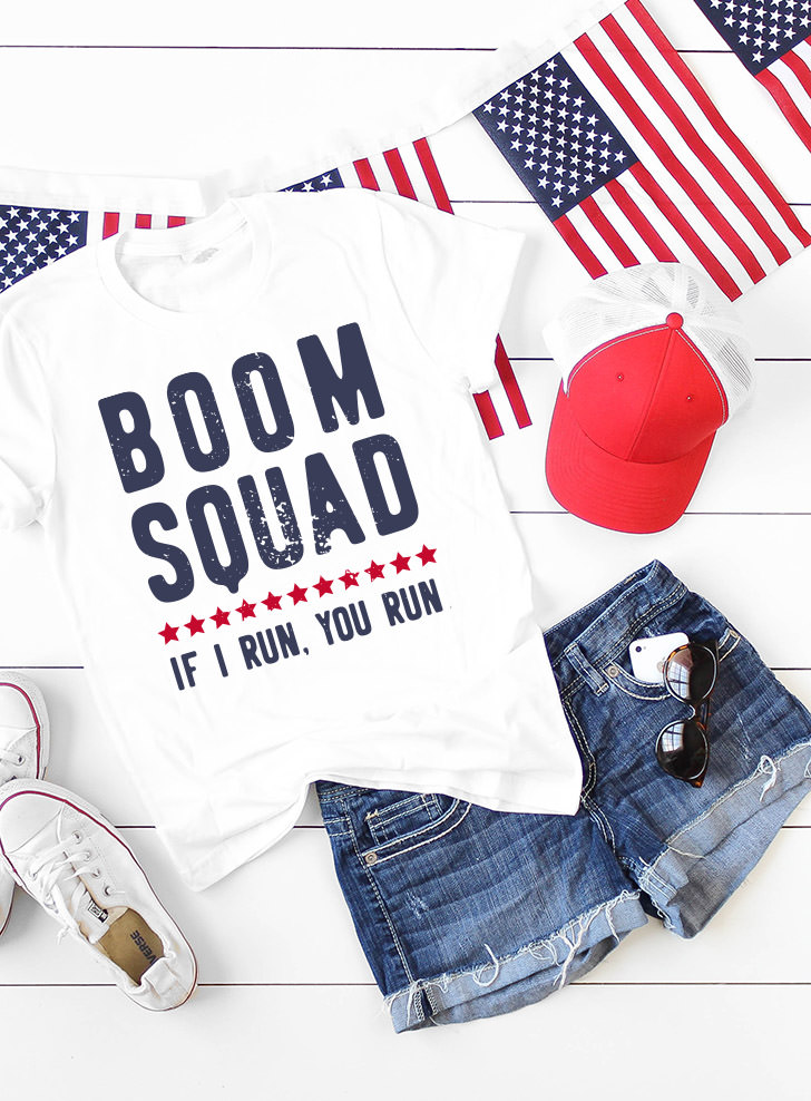 A USA flag banner, a white and red baseball cap, a pair of tennis shoes, a pair of blue jean shorts and a white t-shirt that says, "Boom Squad - If I Run, You Run"