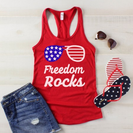 A pair of sunglasses, flip flops, blue jean shorts and a red tank top that says. "Freedom Rocks"