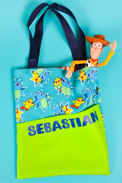 Tote bag that is personalized with a boy's first name and has Woody from the Toy Story movie sticking out of the top of the tote