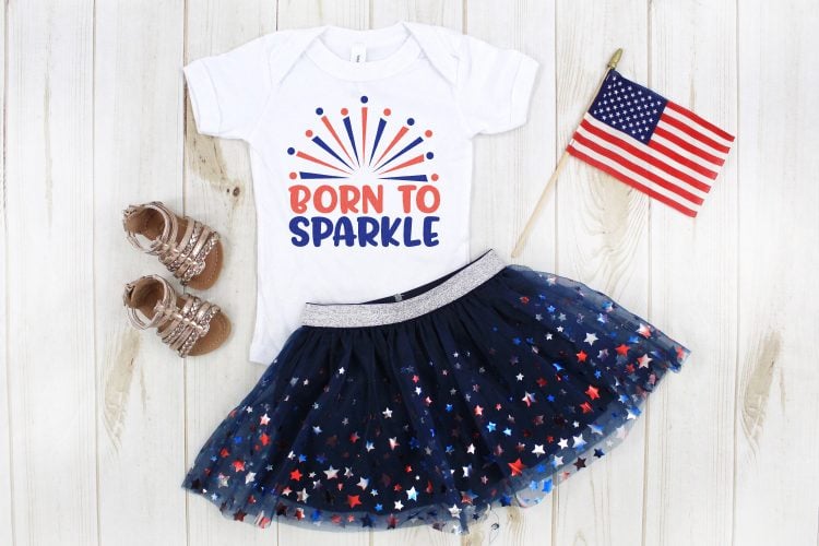 A pair of little girls sandals, an American flag pennant a blue sparkly tutu and a white t-shirt, that says, \"Born to Sparkle\"