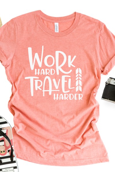 A partial image of a flip-flop and a camera by a pink t-shirt that says, "Work Hard Travel Harder"