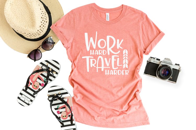 A sun hat, a pair of flip-flops and a camera alongside of a pink t-shirt that says, \"Work Hard Travel Harder\"