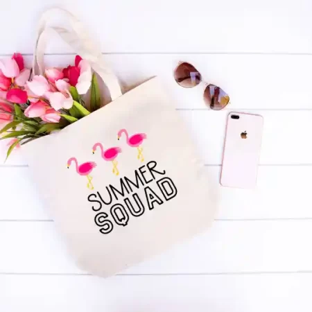 A white tote bag decorated with three flamingos and the saying Summer Squad on it