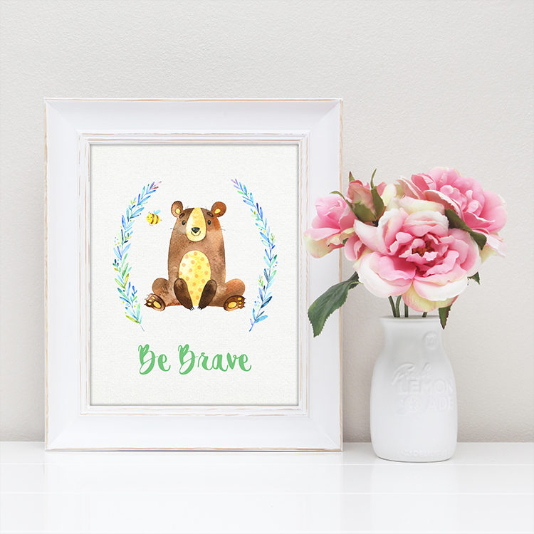 A vase of flowers on a table with a white framed picture of a bear and a bee that says, \"Be Brave\"