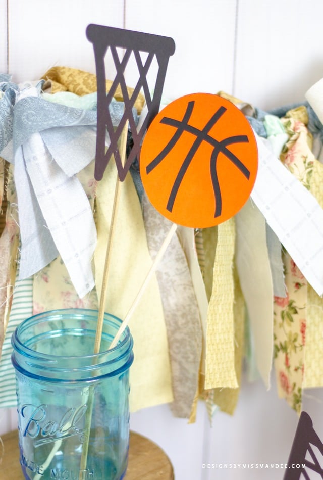 An aqua blue Ball brand canning jar with sticks in it with a cut out of a basketball and a basketball net attached to the sticks 