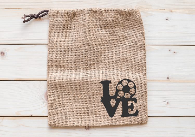 On a white table lies a canvas style drawstring bag decorated in the bottom right-hand corner with the word Love