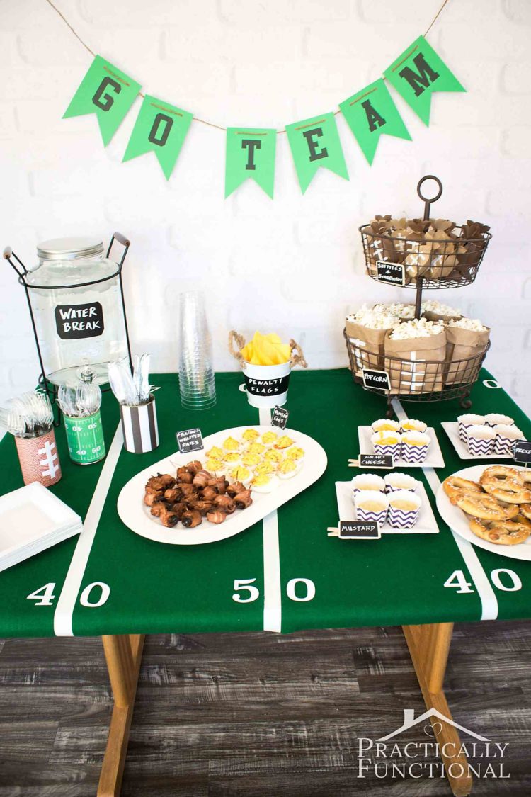 A table decorated with a football field 50-yard line tablecloth and game day food with a Go Team banner hanging above it