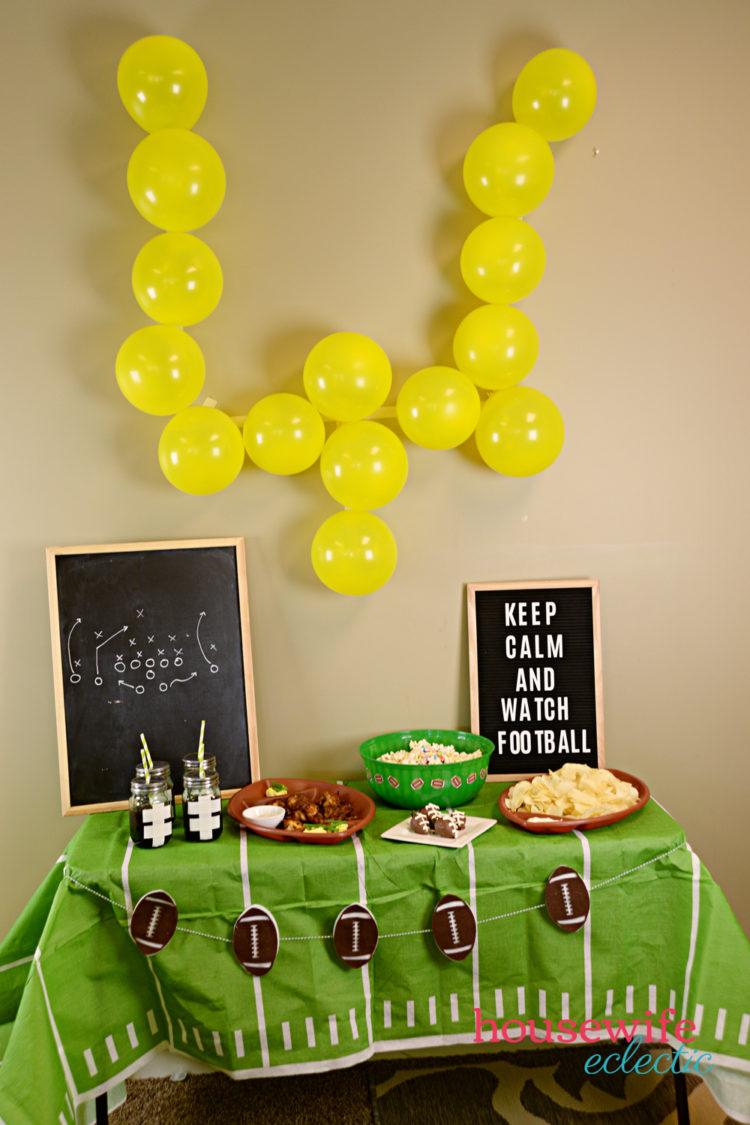 Yellow balloons on the wall shaped as a football goal post, a table decorated with football themed decor and food, and two signs, one with the symbols of the play and one with the saying, \"Keep Calm and Watch Football\"