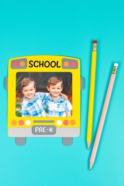 A picture of two adorable little boys is encased in a school bus frame and there are two pencils lying next to the frame