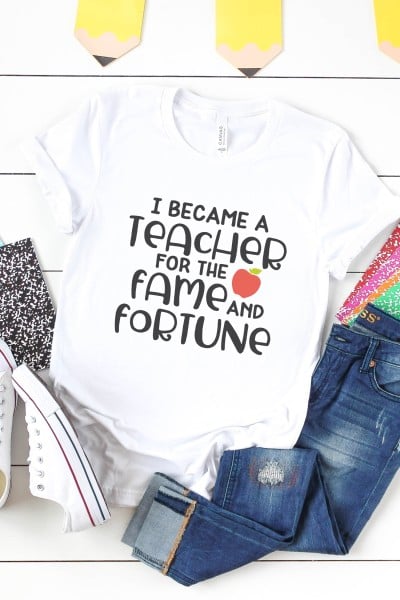 Notebooks, a pair of tennis shoes, a pair of blue jeans and a white t-shirt with the saying, "I Became a Teacher for the Fame and Fortune"