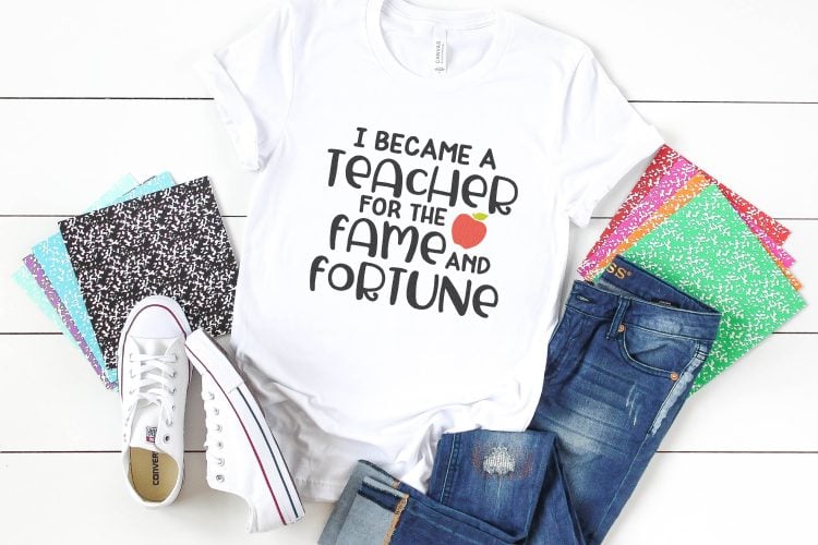 Notebooks, a pair of tennis shoes, a pair of blue jeans and a white t-shirt with the saying, \"I Became a Teacher for the Fame and Fortune\"