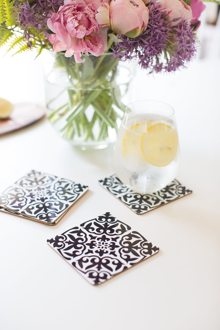 A bouquet of flowers in a vase on a table along-side a set of coasters with a drink sitting on top of one