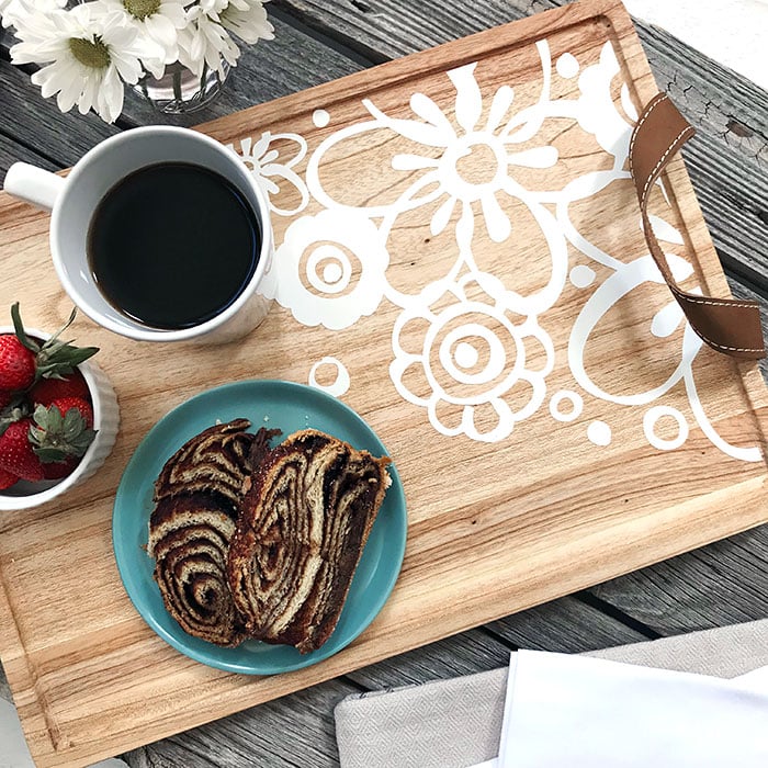 Flowers sitting on a picnic table along with a wooden decorated serving tray that contains a cup of strawberries, a cup of coffee and a serving of cake on a plate 
