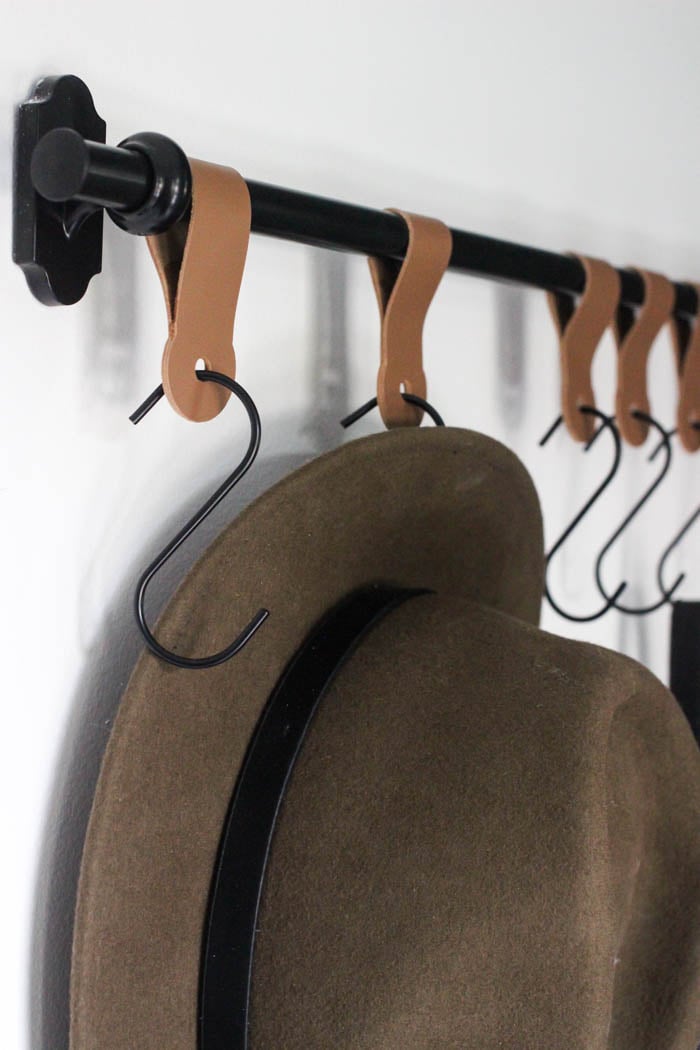 A hat hanging from hooks mounted on a bar attached to the wall