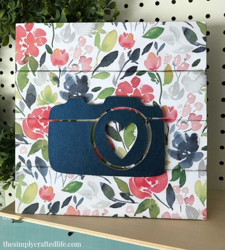 A floral wooden sign with an image of a 3D camera attached to it