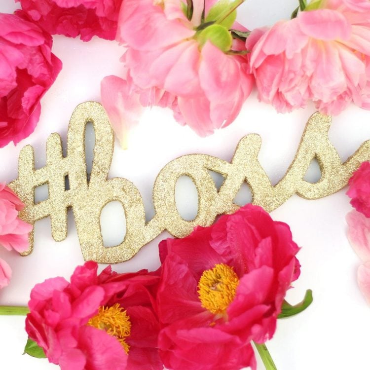 Flowers on a table surrounding a cutout glittery, gold image that says, \"#boss\"