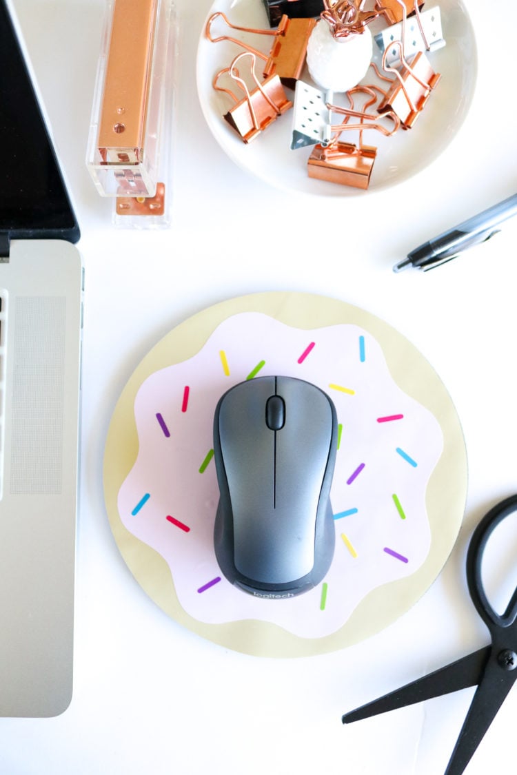 Partial image of a laptop surrounded by a stapler, clips, a pen, a scissors and a wireless mouse on top of a decorated mouse pad