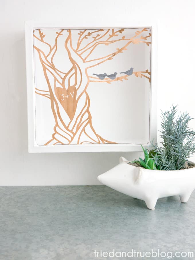 Sitting on a table is an animal shaped vase filled with succulents and above the vase is a framed artwork of a customized curved tree
