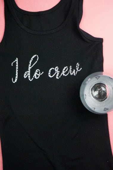 A wine glass and woman's black tank top with the saying, "I Do Crew"