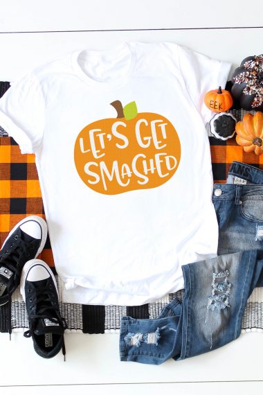 Halloween decor around a pair of blue jeans, a pair of tennis shoes and a white t-shirt that is decorated with an orange pumpkin that says, "Let's Get Smashed"