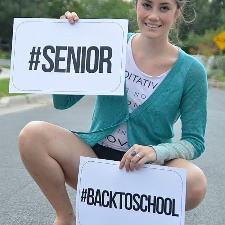 A girl holding two hashtag signs. One says #Senior and the other says #BackToSchool