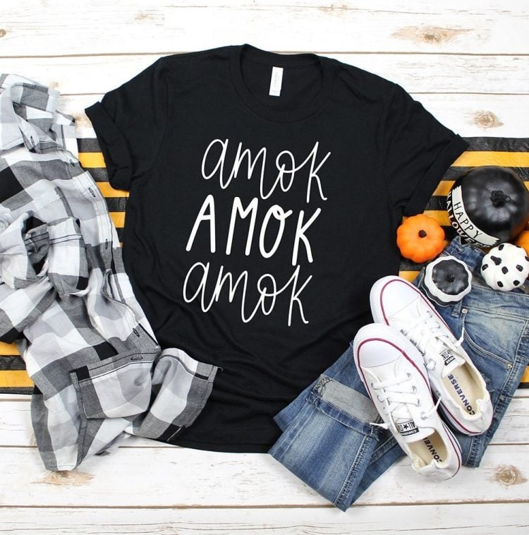 Halloween decor next to a white and black checkered shirt, a pair of tennis shoes, blue jeans and a black t-shirt with the saying, \"AMOK AMOK AMOK\" on it