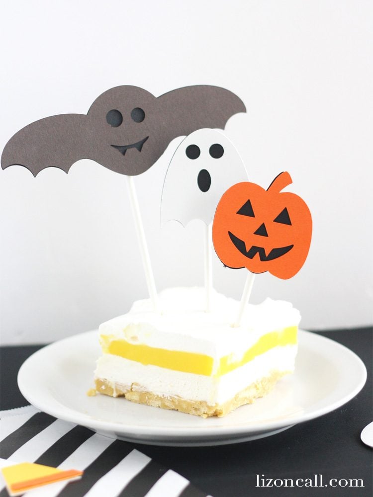 A piece of cake on a plate, with a purple bat, ghost and orange pumpkin cutouts around it