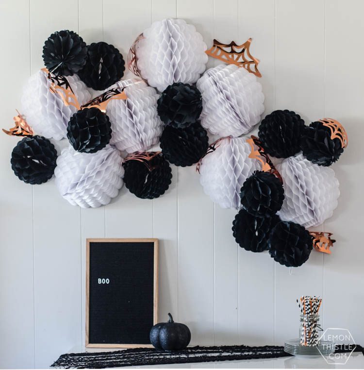 Halloween decor on a table that includes a framed picture with a black background with the word \"BOO\" on it and a giant Halloween garland hanging on the wall