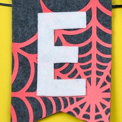 Halloween banner made of grey felt with an orange spider web and the letter "E" cut out of white vinyl