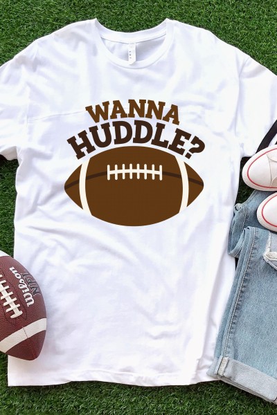 A football, a pair of blue jeans, a pair of tennis shoes all lying on green turf along with a white t-shirt designed with a football and the saying, "Wanna Huddle?"