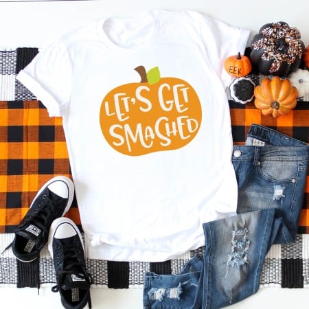 Halloween decor around a pair of blue jeans, tennis shoes and a white t-shirt that is decorated with an orange pumpkin with the saying, "Let's Get Smashed"