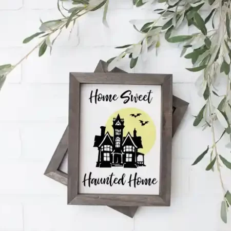 Wooden framed picture with a haunted house on it and the wording Home Sweet Haunted Home