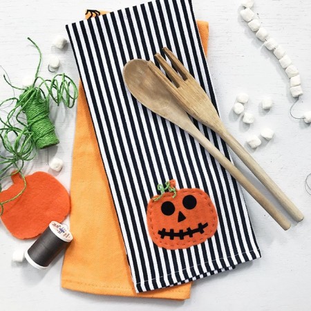 Black and white striped kitchen towel with a felt pumpkin applique handstitched on it