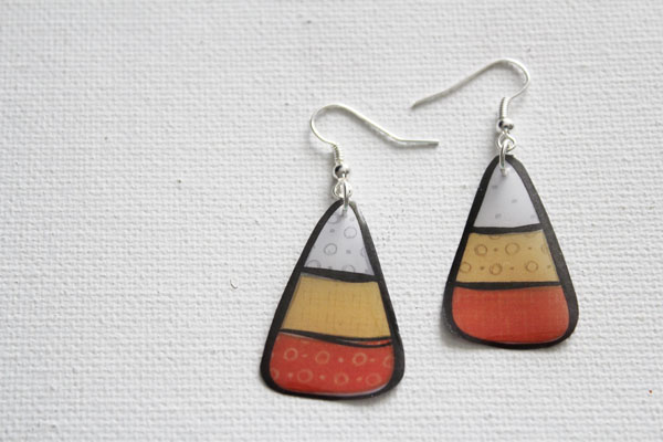 A pair of earrings against a white background that are shaped and the color of candy corn