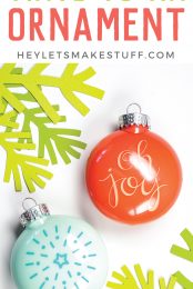 A red Christmas ornament decorated in that white vinyl that says, "Oh Joy" and a blue ornament that displays a radiating star on it in darker blue vinyl with advertising on "How to Apply Vinyl to an Ornament" by HEYLETSMAKESTUFF.COM