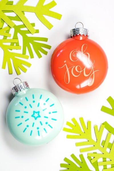 A red Christmas ornament decorated in that white vinyl that says, "Oh Joy" and a blue ornament that displays a radiating star on it in darker blue vinyl