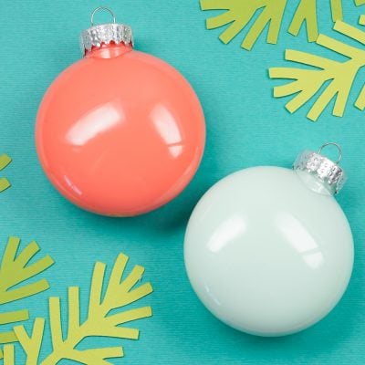 Close up of a white and a peach-colored Ornament next to paper cut greenery