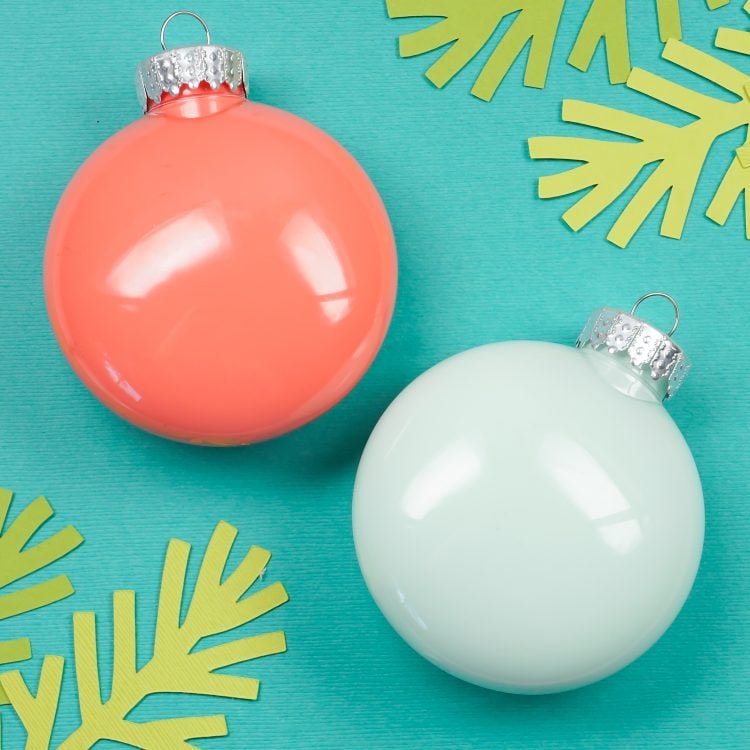 Close up of a white and a peach-colored Ornament next to paper cut greenery