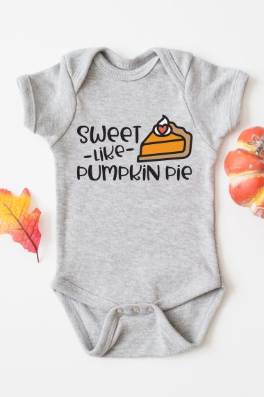 A grey onesie with fall decor around it and the onesie has a design of a piece of pumpkin pie on it with the saying, "Sweet - Like Pumpkin Pie"