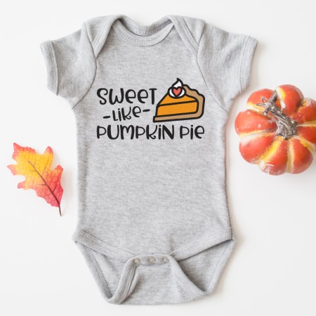 Close-up of a grey onesie with fall decor around it and the onesie has a design of a piece of pumpkin pie on it with the saying, "Sweet - Like Pumpkin Pie"